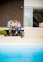 famiglia con un' madre, padre, figlio e figlia seduta al di fuori su passaggi di il nuoto piscina e mangiare fragole foto