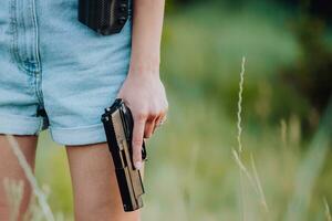 un' ragazza nel denim pantaloncini e con un' pistola nel sua mano pose per un' foto.. avvicinamento foto