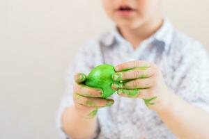 un' bambino detiene un' verde Pasqua uovo nel il suo mani macchiato con dipingere su un' bianca sfondo. foto