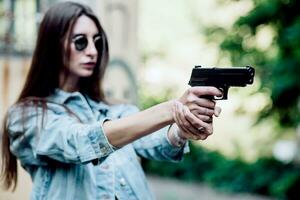 giovane ragazza con un' pistola nel il suo mani spara nel natura foto