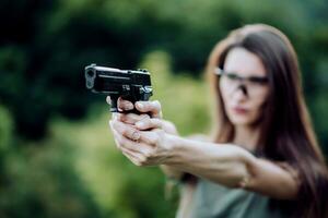 giovane ragazza con un' pistola nel il suo mani spara nel natura foto