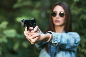 giovane ragazza con un' pistola nel il suo mani spara nel natura foto