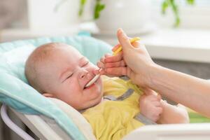 mamma feed il bambino. il bambino piccolo rifiuta per mangiare a partire dal il cucchiaio e socchiude gli occhi. il infantile non lo fa volere per nutrizione. foto