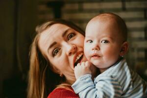 un' madre detiene un' bambino nel sua braccia. mamma abbracci sua bambino che fa i primi passi. ragazza ha divertimento e gioisce con il bambino. un' donna frizioni un' infante. foto