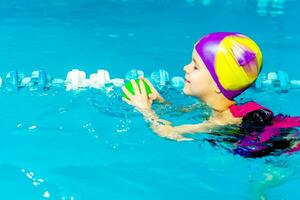 un' poco ragazzo con un' vita giacca su il suo il petto impara per nuotare nel un interno piscina. foto