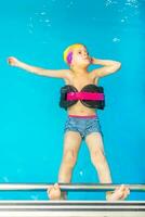 un' piccolo bambino con un' vita giacca su il suo il petto è apprendimento per nuotare nel un interno piscina. foto
