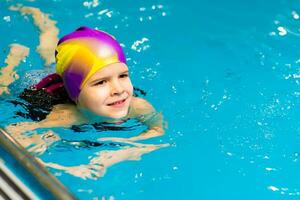 un' piccolo bambino con un' vita giacca su il suo il petto è apprendimento per nuotare nel un interno piscina. foto