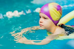 un' poco ragazzo con un' vita giacca su il suo il petto impara per nuotare nel un interno piscina. foto