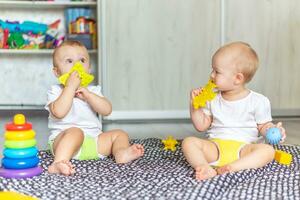 carino contento bambini giocare insieme su il pavimento con giocattoli e prendere loro nel loro bocche foto