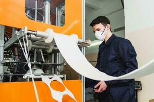 un' lavoratore sta a il macchina nel un' fabbrica per il produzione di medico maschere con nanofibra. coronovirus e covid-19 protezione foto