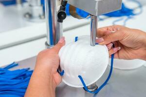 il ragazza lavori nel un' fabbrica per il produzione di medico maschere con nanofibra e saldare loop con ultrasuono su un' macchina. coronavirus e covid-19 protezione.primo piano. foto