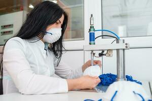 un' donna lavori a un' macchina per il produzione di medico maschere con nanofibra e saldare loop per loro con ultrasuoni. coronovirus e covid-19 prevenzione foto