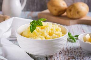 fresco schiacciato patate e basilico le foglie nel un' ciotola su il tavolo foto