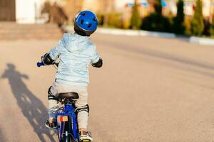 poco ragazzo nel casco cavalcate un' bicicletta su un' soleggiato giorno foto