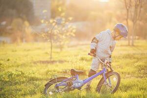 carino bambino è guida un' bicicletta su un' soleggiato giorno a tramonto foto