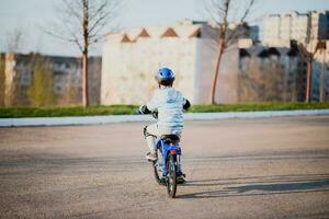 poco ragazzo nel casco cavalcate un' bicicletta su un' soleggiato giorno foto