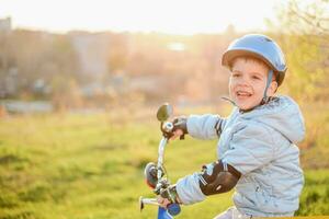 un' bambino nel un' casco impara per cavalcata un' bicicletta su un' soleggiato giorno a tramonto foto