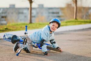 un' poco ragazzo nel un' casco abbattere a partire dal un' bicicletta su il asfalto e era non ferito foto