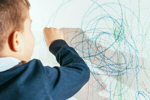 il bambino disegna su il parete con un' pastello. il ragazzo è impegnato nel creatività a casa foto