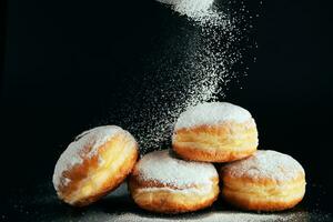 in polvere zucchero è versato su ciambelle. tradizionale ebraico dolce sufganiyot su nero sfondo. cucinando fritte berlinesi. foto