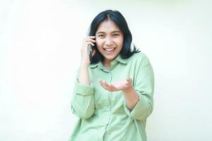 spensierato Contentissimo asiatico donna indossare verde al di sopra di dimensione camicia godere A proposito di su telefono con raccolta palme mostrando presentazione gesto in piedi al di sopra di isolato bianca sfondo, guardare a telecamera foto