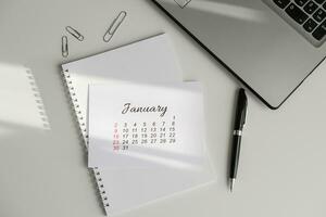 gennaio calendario, bloc notes e il computer portatile su il ufficio tavolo foto