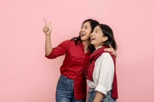 bellissimo asiatico donna nel rosso camicia puntamento per Spedire Messaggio isolato attraente e allegro asiatico donne abbracciare ogni altro su rosa sfondo. foto