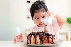 4-5 anno vecchio ,carino asiatico ragazza è Sorridi e scrosciante cioccolato su cioccolato crostini su bianca tavolo nel un' caffè fai la spesa, tesoro crostini è un' dolce dolce quello bambini amore, rilassare contento famiglia tempo concetto foto