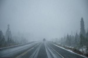 guida in auto in caso di neve pesante sull'autostrada nella foresta di pini al parco nazionale di Banff