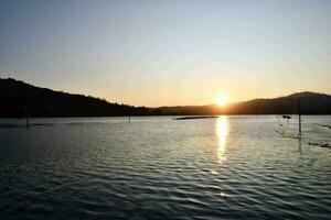 il sole imposta al di sopra di un' lago con un' barca nel il acqua foto