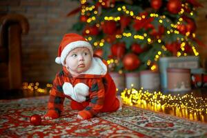 poco contento ragazza di 6 mesi brividi vicino un' nuovo anno albero su Natale vigilia. bambino nel Santa Claus costume vicino luminoso ghirlande. contento nuovo anno 2020 concetto foto