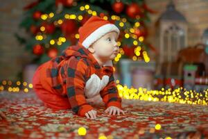 poco contento ragazza di 6 mesi brividi vicino un' nuovo anno albero su Natale vigilia. bambino nel Santa Claus costume vicino luminoso ghirlande. contento nuovo anno 2020 concetto foto