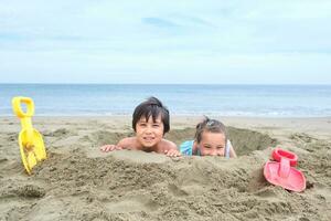 bambini scavare un' buco nel il sabbia su il spiaggia. foto