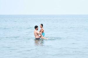 papà giochi con il suo figli maschi nel il mare. foto