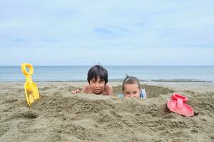 bambini scavare un' buco nel il sabbia su il spiaggia. foto
