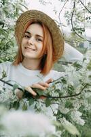 ritratto di un' donna nel un' cannuccia cappello nel un' ciliegia fiore. gratuito all'aperto ricreazione, primavera fioritura giardino. foto