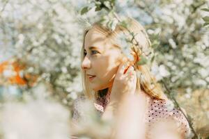 bionda ragazza su un' primavera camminare nel il giardino con ciliegia fiori. femmina ritratto, avvicinamento. un' ragazza nel un' rosa polka punto vestire. foto