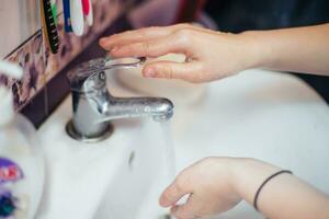 bambino si chiude rubinetto con fluente acqua. Salvataggio acqua. pulizia mano per fermare diffusione di covid-19, coronavirus pandemia foto