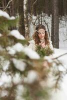 bellissimo sposa nel un' bianca vestito con un' mazzo nel un' innevato inverno foresta. ritratto di il sposa nel natura. foto