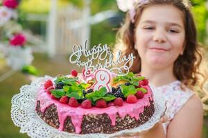 ragazza Tenere compleanno torta con numero 8 e iscrizione contento compleanno. festeggiare cerimoniale eventi su strada durante quarantena. bambino nel sfondo decorato foto zona di fiori.