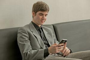 giovane uomo legge notizia e Guardando video su smartphone. tipo detiene Telefono nel mani e colpi attraverso schermo con dito. foto
