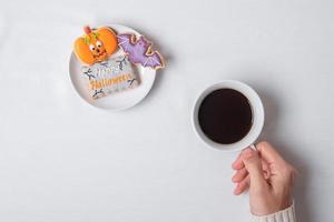 mano della donna che tiene la tazza di caffè durante il consumo di biscotti divertenti di halloween. buon giorno di halloween, trucco o minaccia, ciao ottobre, autunno autunno, tradizionale, festa e concetto di vacanza foto