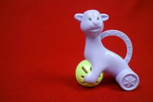 un' giocattolo sagomato piace un alpaca animale, viola colore, Tenere un' sfera. su un' rosso sfondo foto