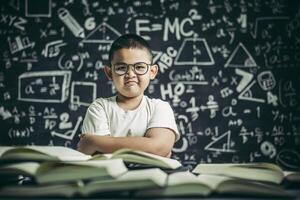 un ragazzo con gli occhiali seduto in classe a leggere foto