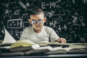 un ragazzo con gli occhiali seduto in classe a leggere foto