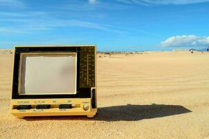 un' piccolo giallo televisione seduta nel il sabbia foto