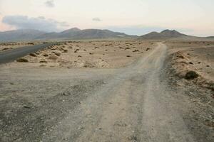 un' sporco strada nel il mezzo di un' deserto con montagne nel il sfondo foto