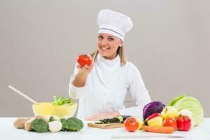 femmina capocuoco mostrando pomodoro mentre fabbricazione salutare pasto foto