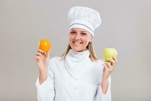 bellissimo femmina capocuoco è mostrando frutta su grigio sfondo. foto