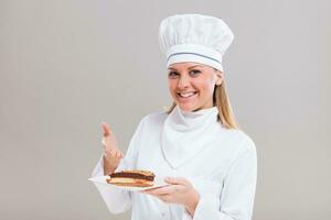 bellissimo femmina pasticciere è mostrando fetta di torta su grigio sfondo. foto